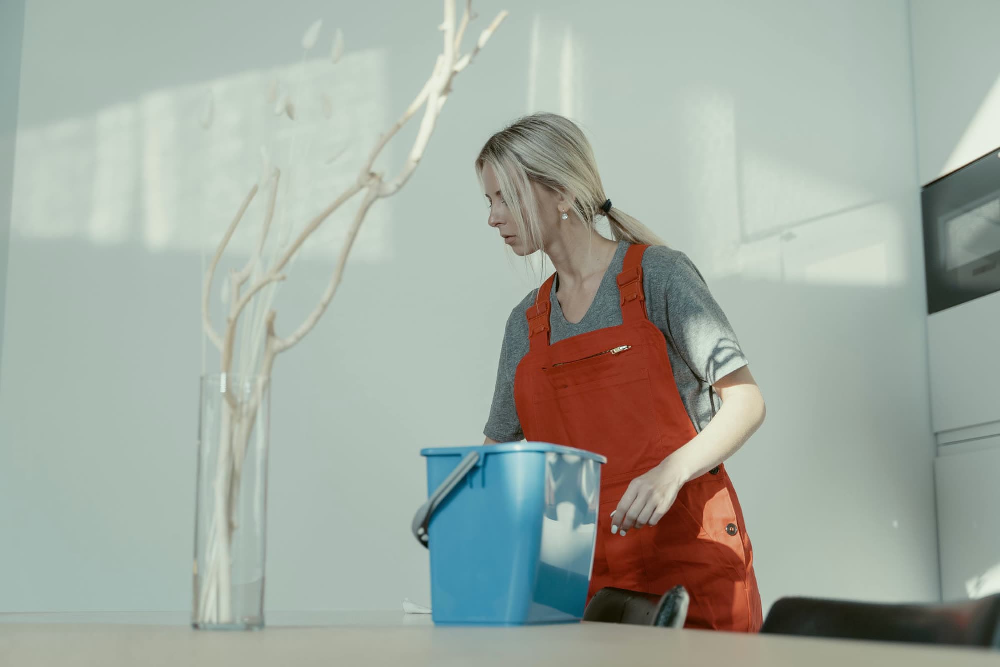 A cleaner in an orange jumpsuit at work in a home, with a blue bucket.