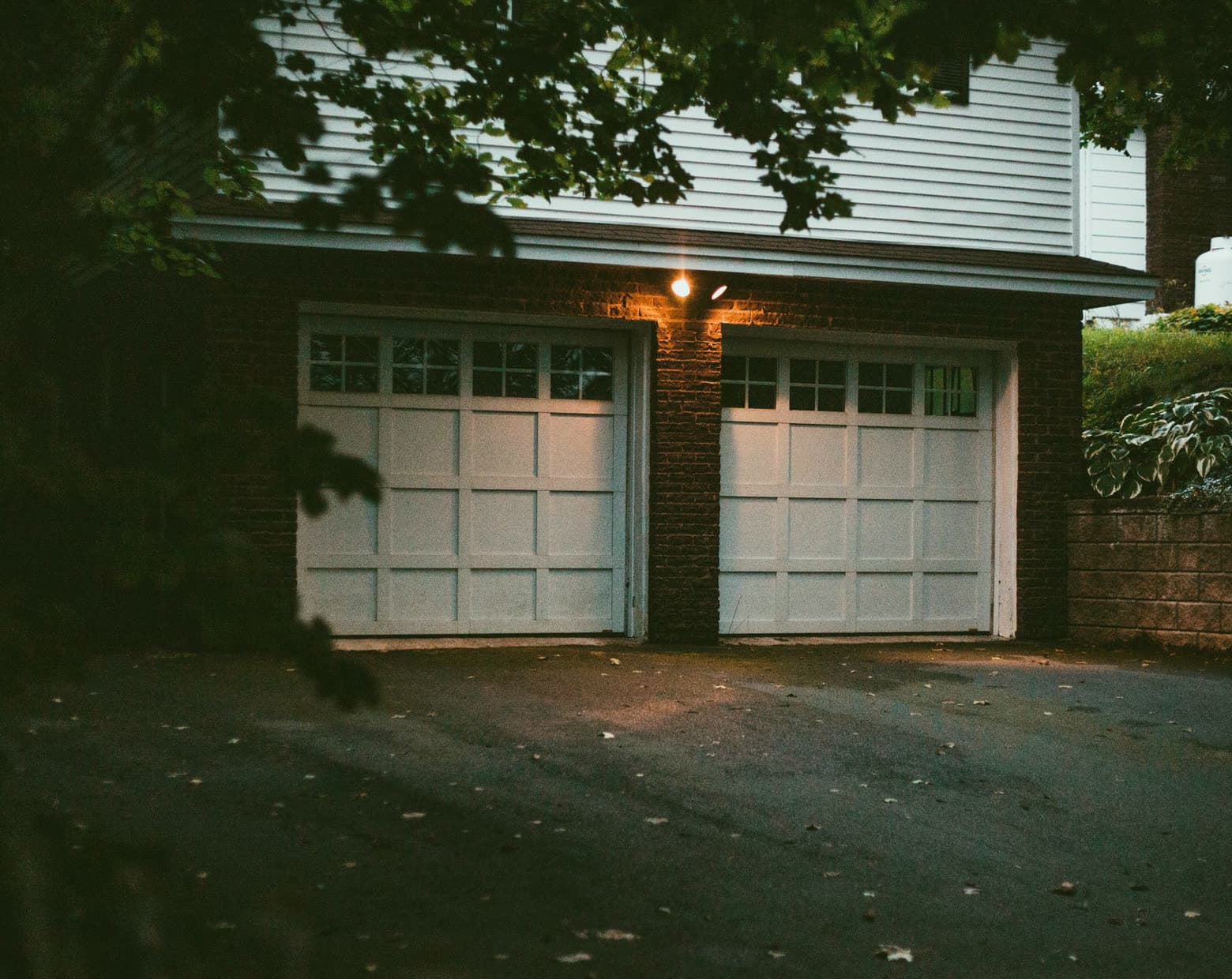 A brick double garage with white panelled doors under a porch light at dusk.